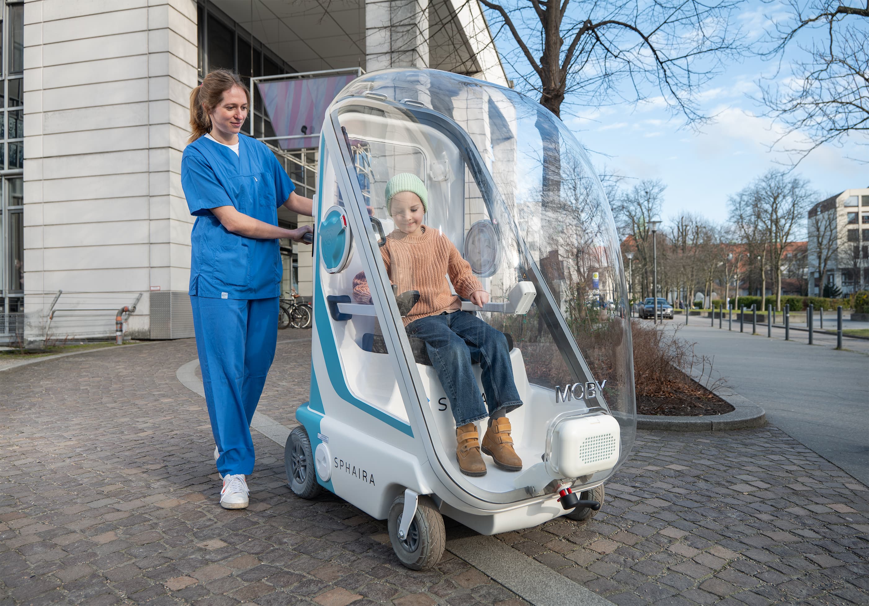 Nurse pushing a child in a MOBY pod outside a hospital